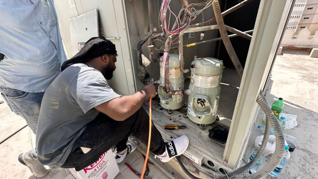 Technician servicing twin compressors on a rooftop package AC unit in International City, Dubai